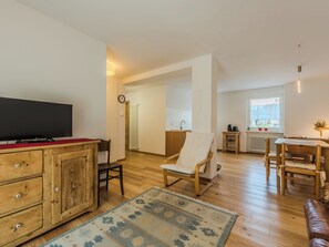 A modern living room with a flat-screen TV, wooden furniture, a patterned rug, and a view of the outside.