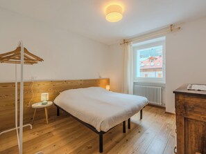 A bedroom with a wooden headboard, a bed, a bedside table with a lamp, a window with curtains, and a radiator. - La Casa di Bruna by Interhome (Spiazzo)