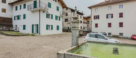 Una calle empedrada con edificios, una fuente y coches aparcados.