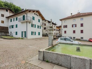 A cobblestone street with buildings, a fountain, and parked cars. - La Casa di Bruna by Interhome (Spiazzo)