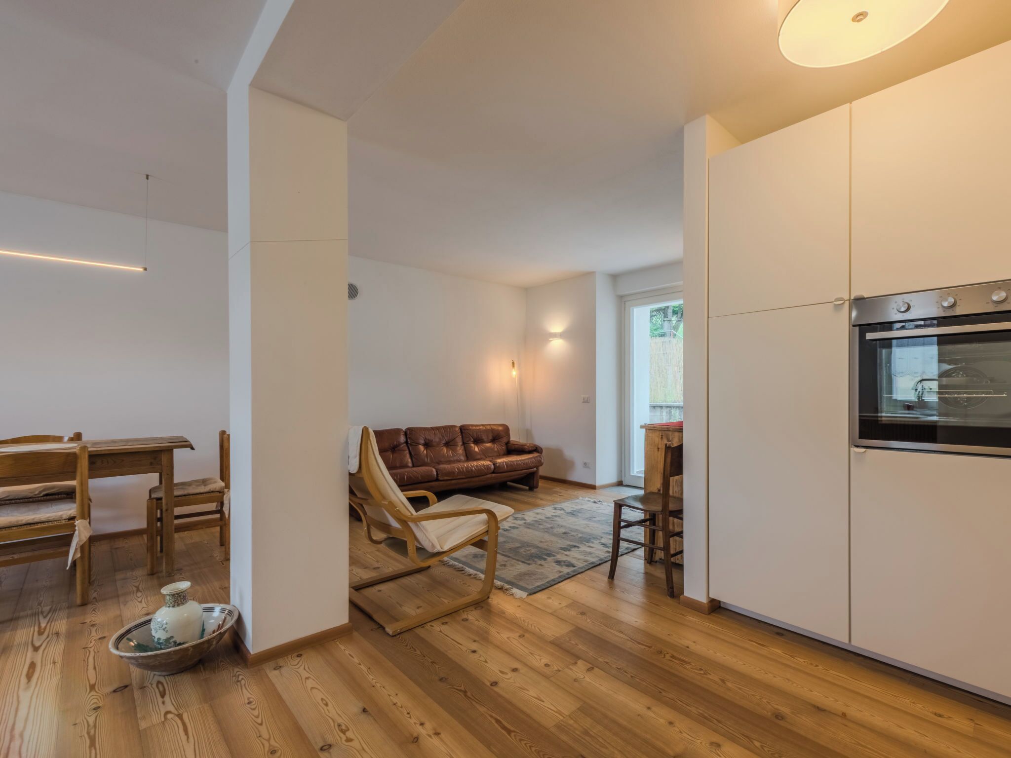 A modern kitchen with wooden flooring, a dining area with a wooden table and chairs, a brown leather sofa, and a large oven.