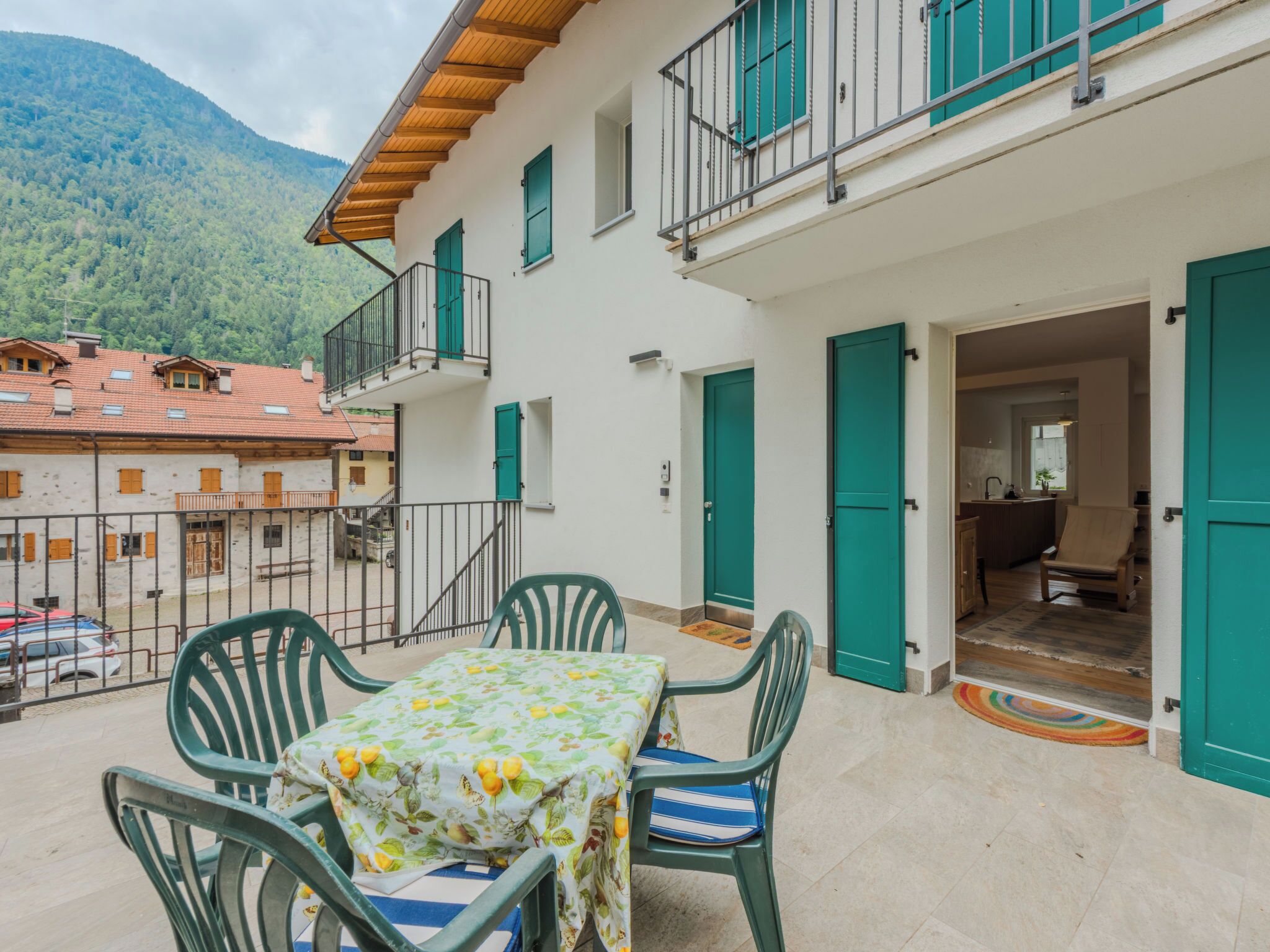 A two-story building with a balcony, a dining table with chairs, and a view of a mountain.