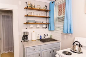 A compact kitchen with a coffee maker, kettle, sink, and storage cabinets.
