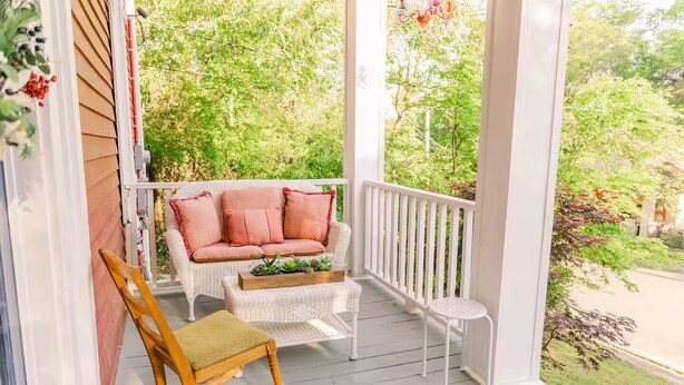 A porch with a wicker sofa, a wooden rocking chair, and a small table.