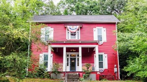 A red house with a front porch, white trim, and a number '110' on the door.