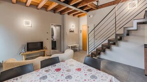 Un intérieur moderne avec des poutres apparentes, un escalier, un téléviseur à écran plat, un canapé et une nappe à motifs.