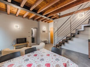 A modern interior with exposed wooden beams, a staircase, a flat-screen TV, a sofa, and a patterned tablecloth. - Apartment Silvia by Interhome (Caderzone Terme)
