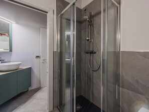 Un baño moderno con ducha envuelta en vidrio, lavabo con mueble y espejo sobre él.