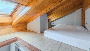 Une chambre avec un plafond en bois incliné, un puits de lumière et un lit.