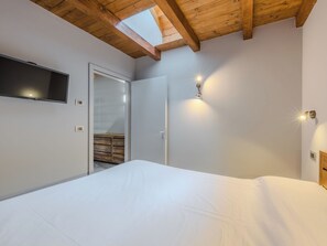 Un dormitorio con cama, televisor montado en la pared y tragaluz.