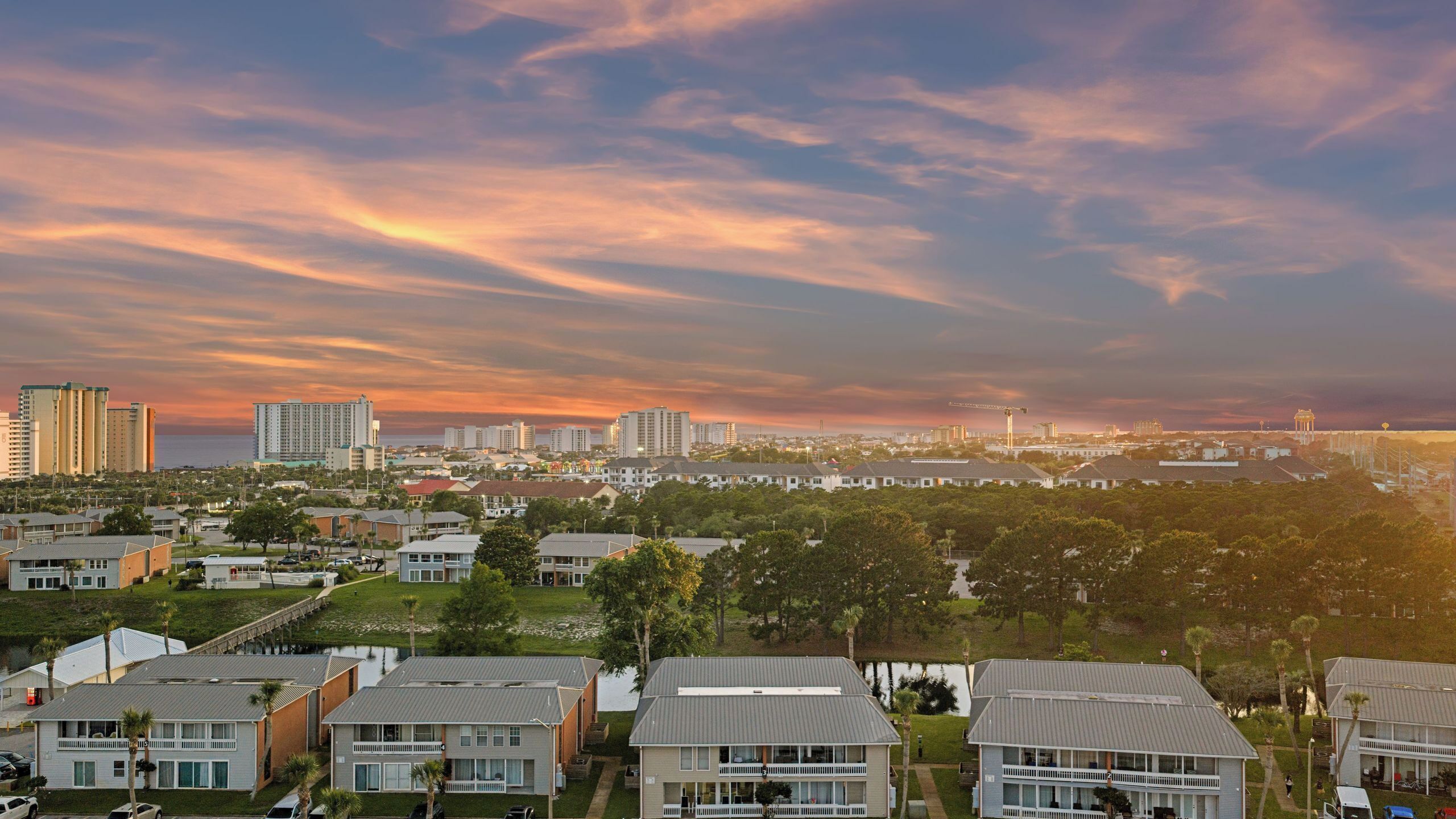 A coastal cityscape with residential buildings, a marina, and high-rise buildings under a sunset sky.
