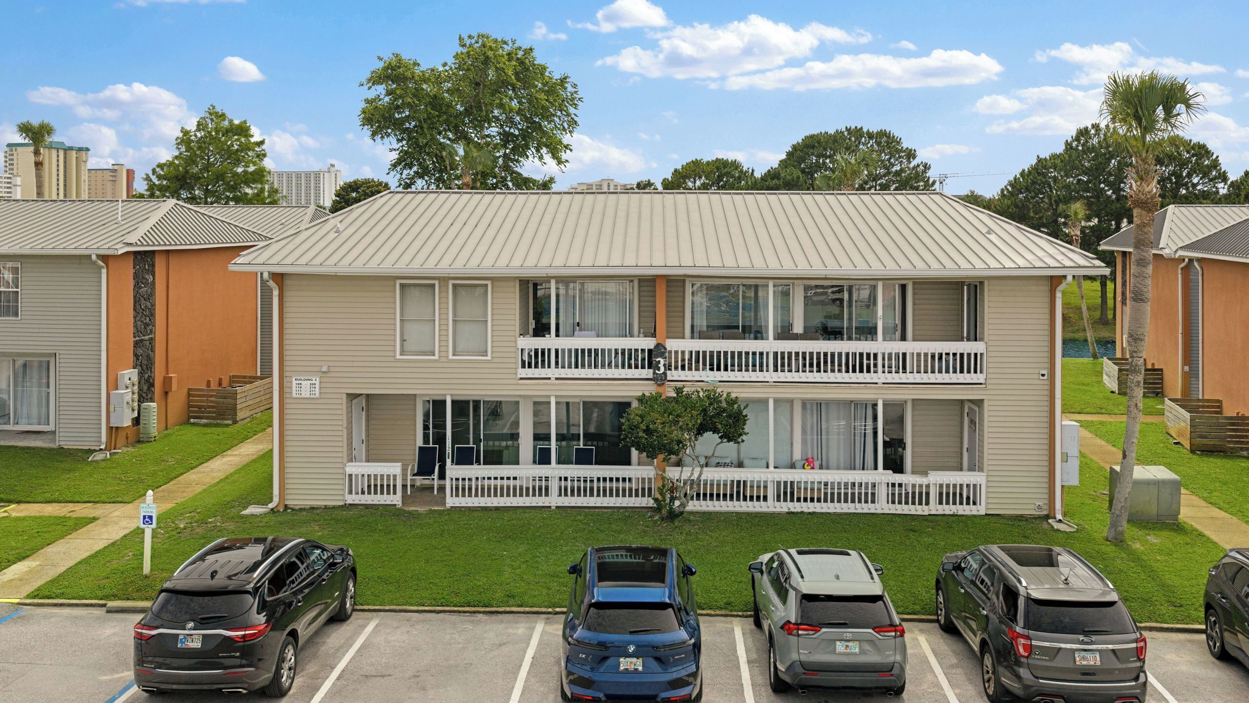 A two-story building with a flat roof, a front porch with a white railing, and a parking lot with several cars.
