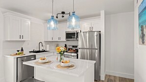 Uma cozinha moderna com armários brancos, eletrodomésticos de aço inoxidável e uma ilha central com alimentos.