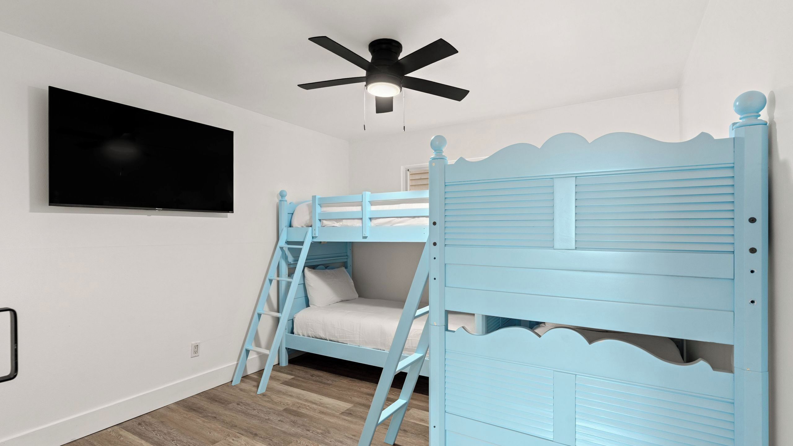 Een slaapkamer met stapelbedden, een plafondventilator, een televisie aan de muur en een houten vloer.