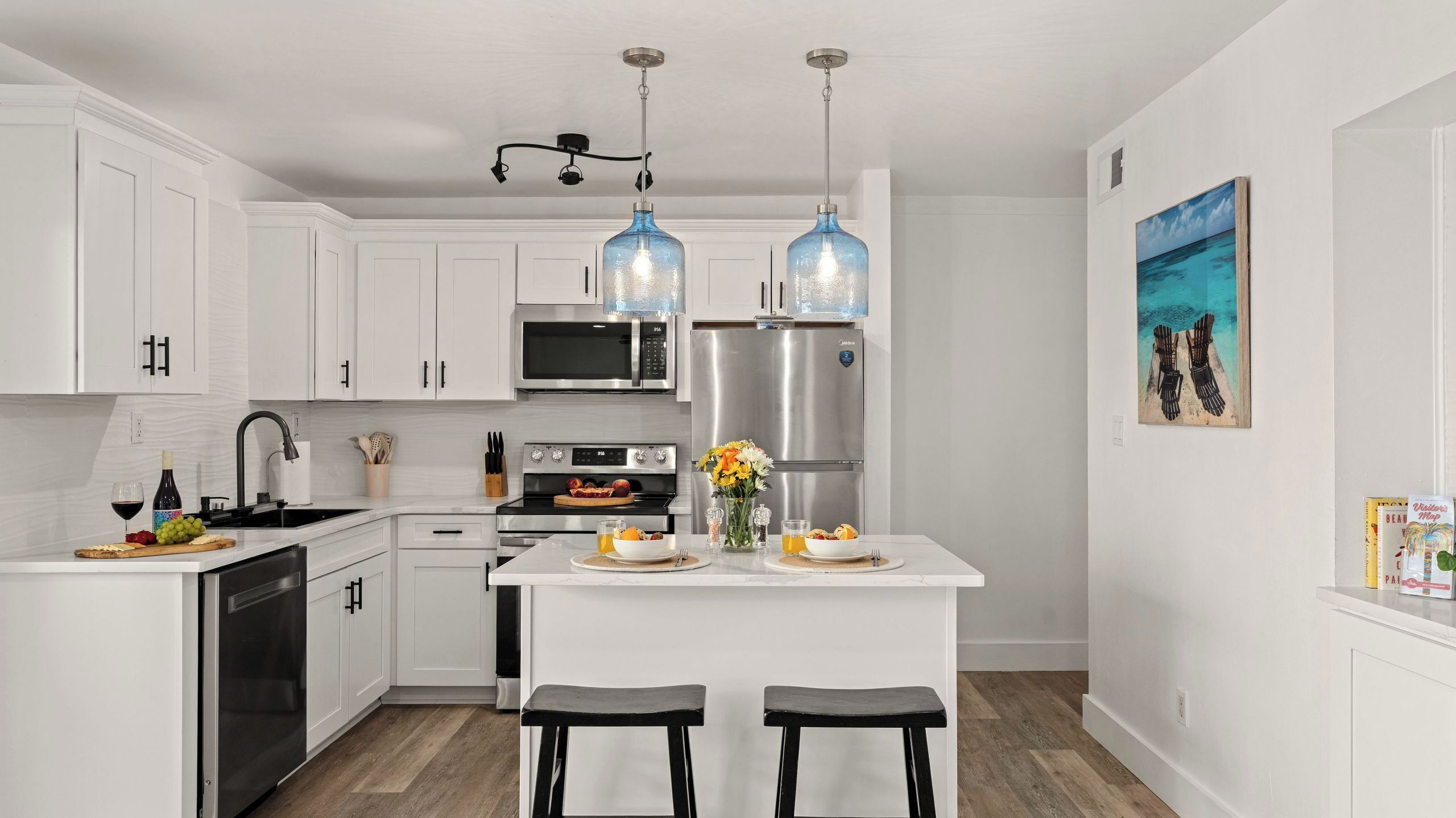 A modern kitchen with white cabinetry, stainless steel appliances, and a central island with seating.