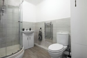 A modern bathroom with a glass shower enclosure, a white sink, a toilet, and a towel rack. - The Rushden Retreat • 1-Bed Flat + Parking (Rushden)