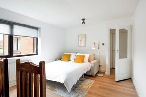 A bedroom with a bed, a chair, a bedside table, a lamp, and a door.