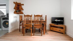 A dining area with a wooden table and chairs, a TV on a wooden stand, and a laundry machine in the background. - The Rushden Retreat • 1-Bed Flat + Parking (Rushden)