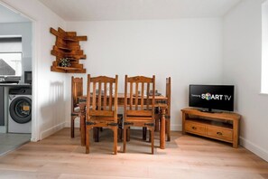 A dining area with a wooden table and chairs, a TV on a wooden stand, and a laundry machine in the background.