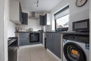A compact kitchen with grey cabinets, a built-in oven, a microwave, and a washing machine.