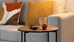 A modern living room with a sofa, a small round table, a remote control, a glass of water, and an apple. - The Rushden Retreat • 1-Bed Flat + Parking (Rushden)