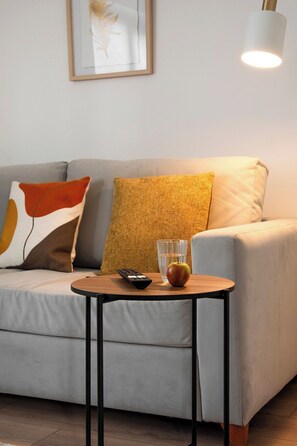 A modern living room with a sofa, a small round table, a remote control, a glass of water, and an apple.
