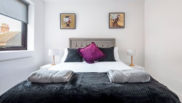 A bedroom with a bed, two wall-mounted lamps, a window, and two framed artworks on the wall. - The Rushden Retreat • 1-Bed Flat + Parking (Rushden)