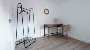 A room with a metal clothes rack, a wooden desk, a chair, and a wall-mounted lamp. - The Rushden Retreat • 1-Bed Flat + Parking (Rushden)