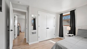 Un dormitorio con cama, mesita de noche, espejo, armario y pasillo que conduce a otra habitación.