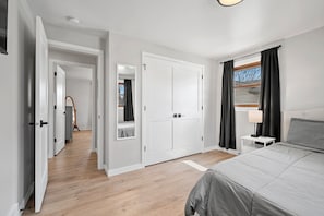 A bedroom with a bed, a nightstand, a mirror, a wardrobe, and a hallway leading to another room.