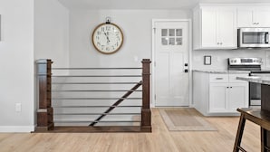 Una cocina con armarios blancos, un microondas de acero inoxidable y una escalera de madera.