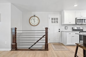 A kitchen with white cabinets, a stainless steel microwave, and a wooden staircase.
