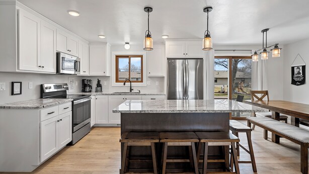 Una cocina moderna con armarios blancos, electrodomésticos de acero inoxidable y una isla central con taburetes de bar.