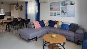 A modern living room with a grey sectional sofa, a round wooden coffee table, and a dining area with a table and chairs. - Villa Seka (Rogoznica)