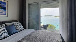 A bedroom with a bed, a chair, a painting, and a view of the sea. - Villa Seka (Rogoznica)