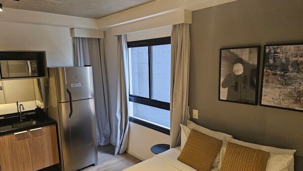 Una camera d'albergo con un letto, un angolo cottura, una finestra con tende e opere d'arte alle pareti.