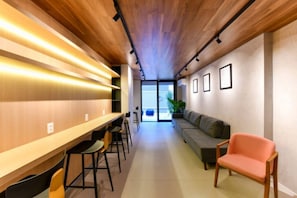 Ein modernes Interieur mit einer langen Holztheke, Barhocker, einer Couch und einem Sessel.