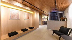 Un interno moderno con soffitto in legno, una reception con cuscini neri e opere d'arte incorniciate al muro.