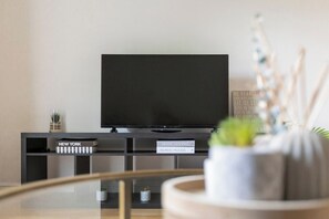 Un soggiorno moderno con una TV nera su un mobile, una piccola pianta in vaso e un oggetto decorativo sullo scaffale.