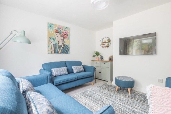 A living room with a blue sofa, a round ottoman, a patterned rug, a floor lamp, a painting, a cabinet, and a television.