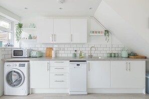 Une cuisine moderne avec des meubles blancs, un lave-linge, un lave-vaisselle et un four à micro-ondes.