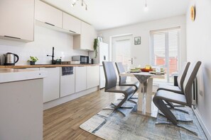 Una cocina moderna con armarios blancos, microondas y cafetera. Hay una zona de comedor con una mesa y sillas.