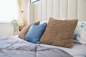 A bed with a white headboard, a grey blanket, and three pillows.