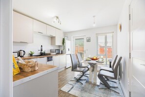 A modern kitchen with white cabinets, a dining area with two chairs, and a small table with a fruit bowl.