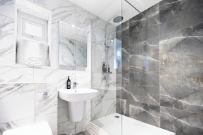 Een moderne badkamer met een douchecabine van glas, een wit wastafelmeubel en marmeren tegels.