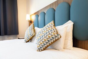 Een hotelkamer met een bed, kussens, een hoofdeinde en een wandlamp.