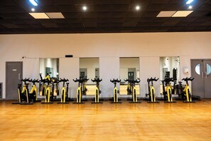 Een sportschool met een rij hometrainers, houten vloeren en spiegels aan de muren.