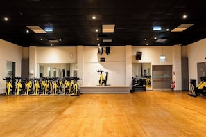 Een ruime fitnessruimte met meerdere hometrainers, een houten vloer en een hoog plafond met ingebouwde verlichting.