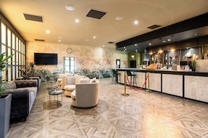Een hotellobby met een bar, zithoekjes en een groot raam dat voor natuurlijk licht zorgt.