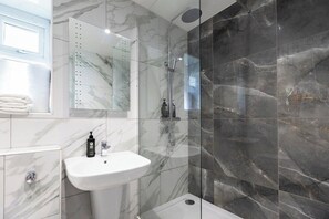 Een moderne badkamer met een douche, wastafel en spiegel.